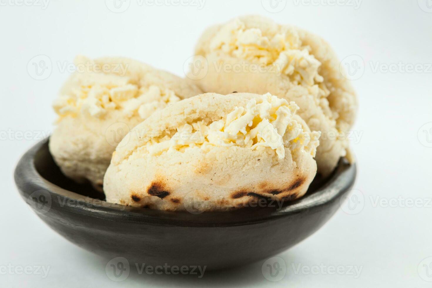 Colombian traditional white corn arepa stuffed with grated cheese in a black ceramic dish on white background photo