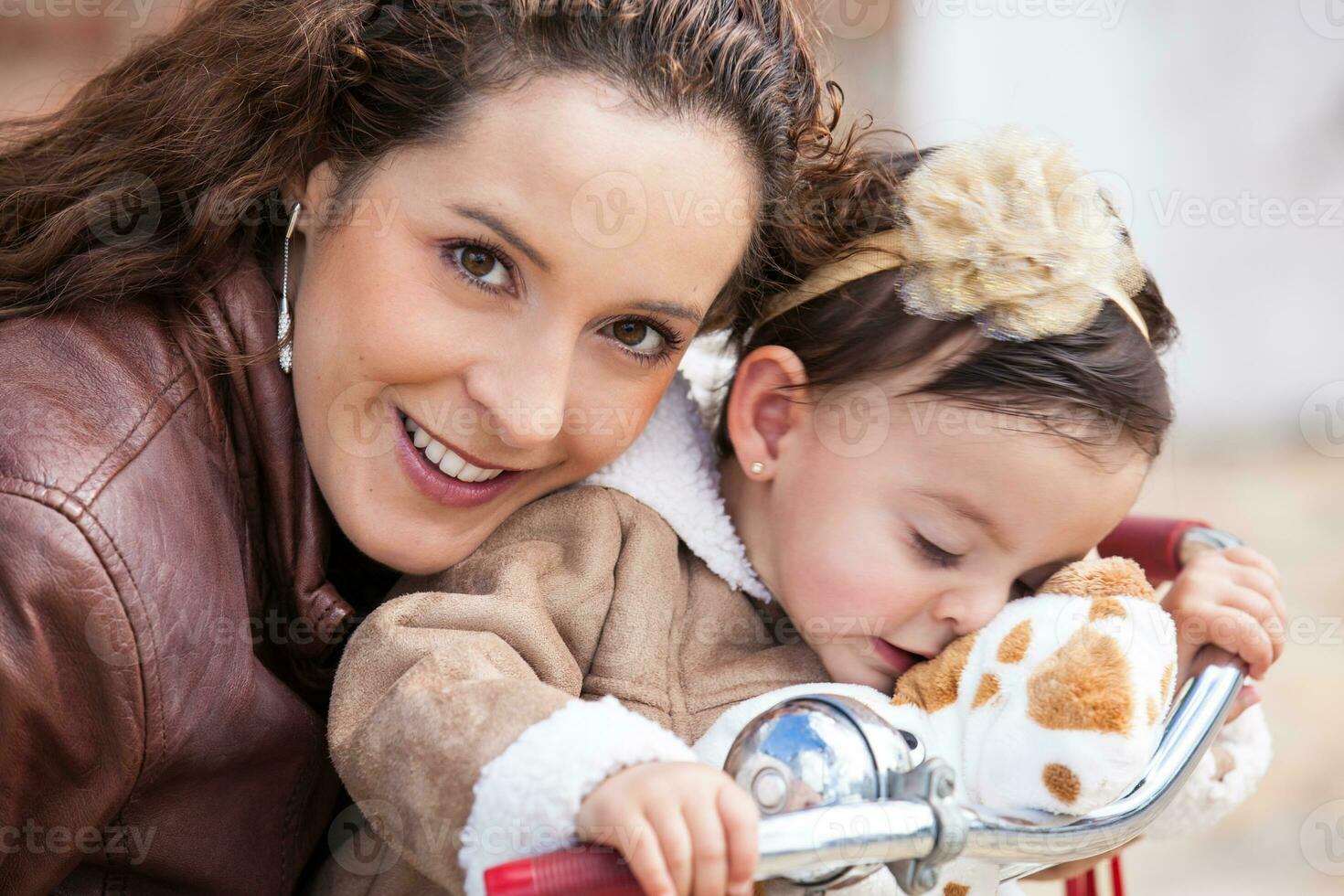 Beautiful young mother playing with her one year old baby outdoors. With mom riding my tricycle photo