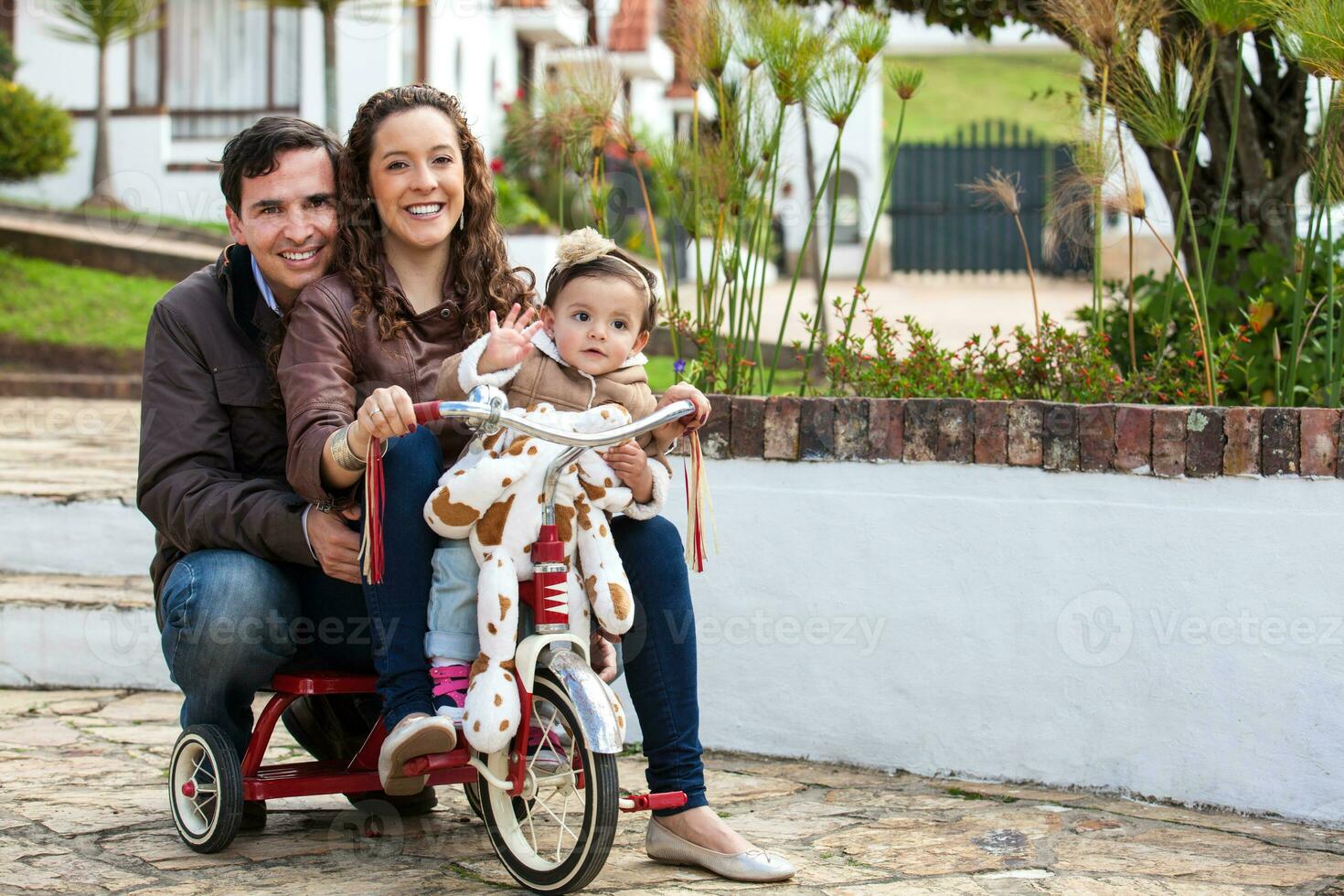 uno año antiguo bebé al aire libre montando su triciclo con su padres. foto