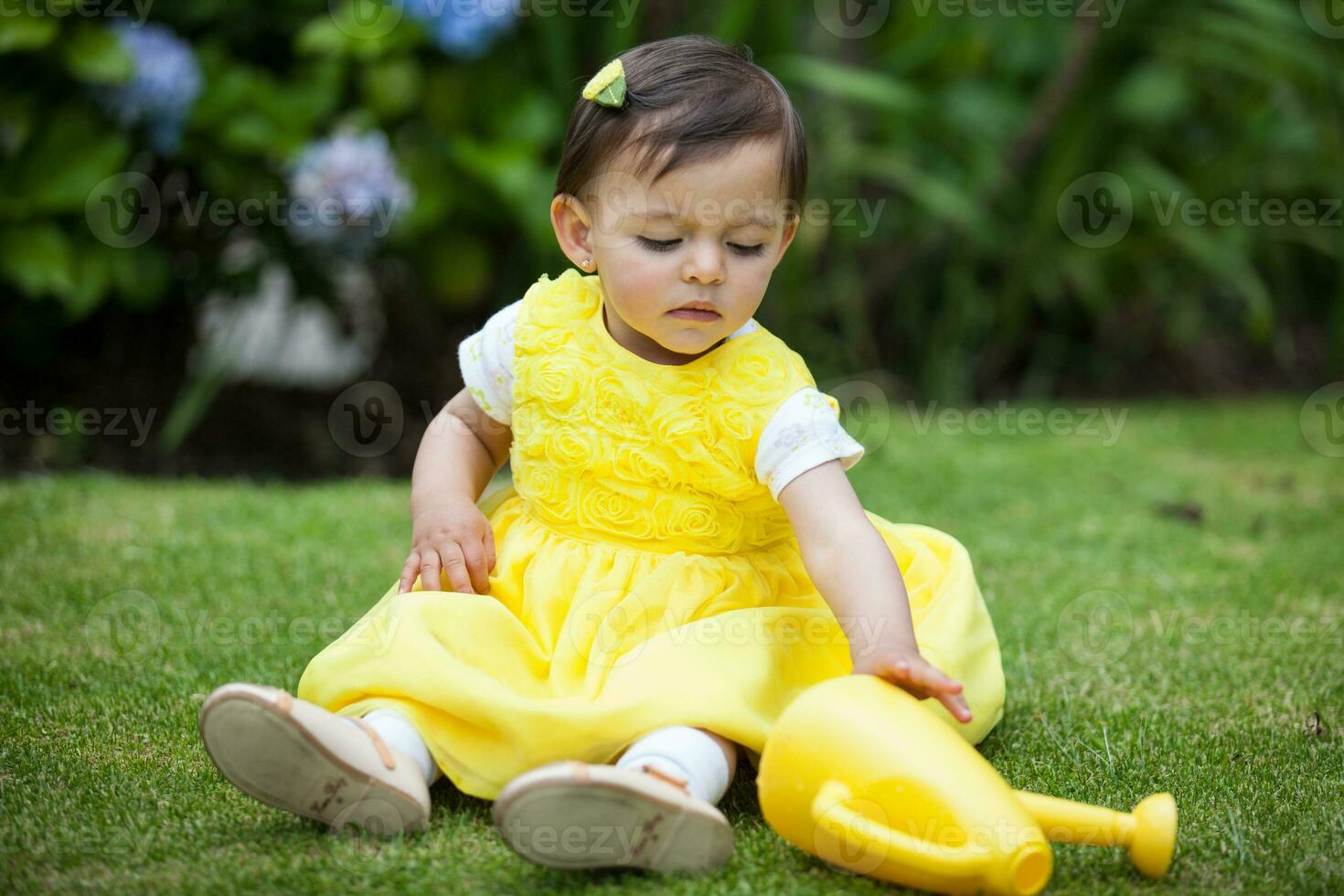 Sweet one year old baby girl dressed in yellow watering the plants at the garden photo