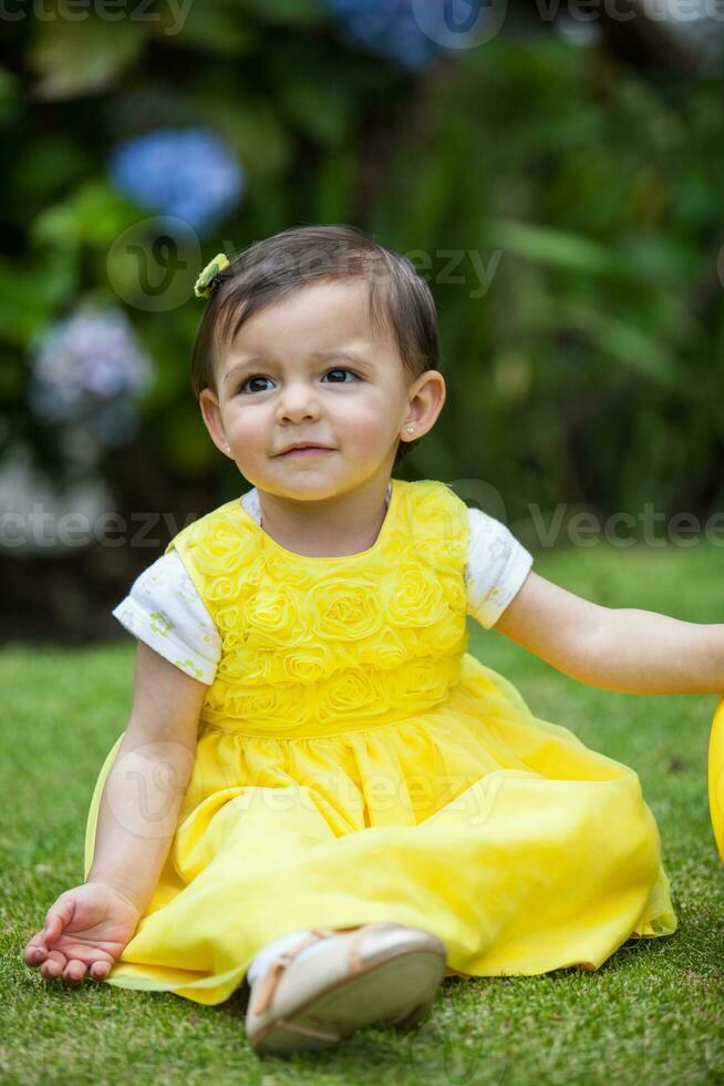 Sweet one year old baby girl dressed in yellow watering the plants at the garden photo