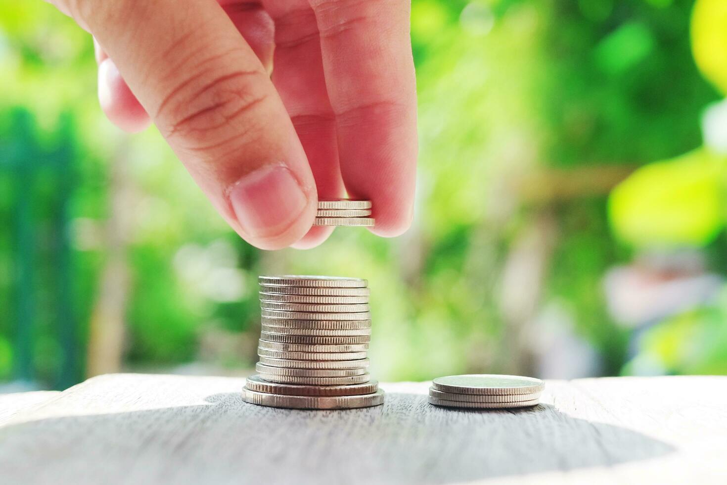 Hand holding Money coins on wooden floor in green natural bokeh background for Saving and growing in success economy and bussiness life concept. photo