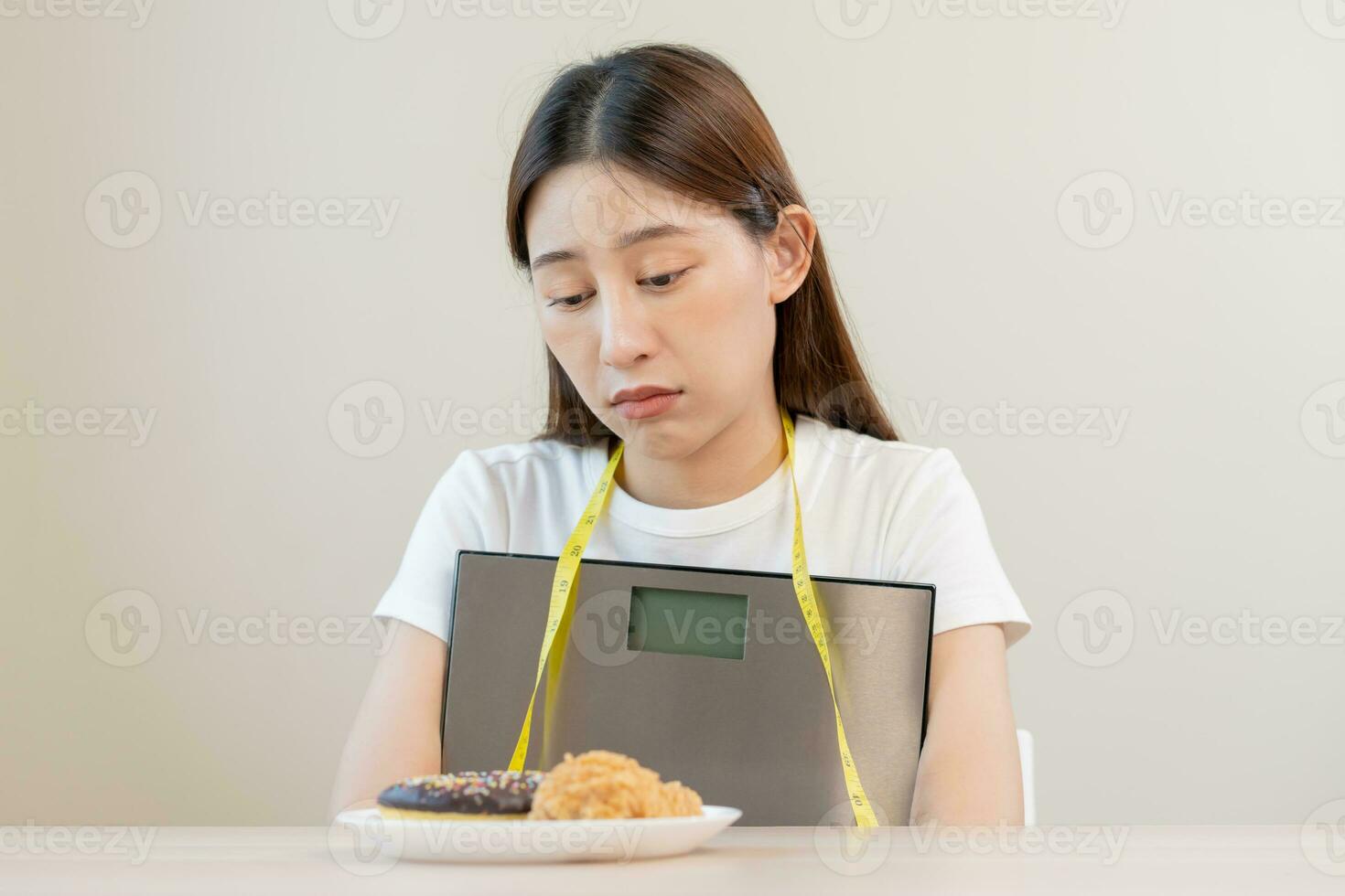 dieta, atractivo asiático joven mujer, niña contenido a comer rosquilla, panadería y frito pollo, rápido comida a perder, pérdida peso, abrazando peso escamas en mesa a hogar. pasión, tentación cuando hambriento. foto