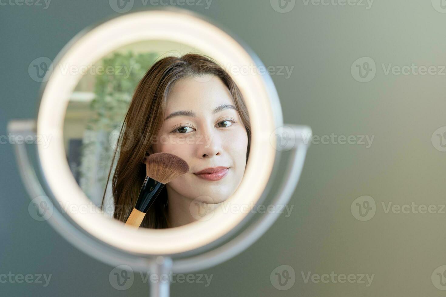 Happy routine beauty concept, pretty asian young woman, girl make up face by applying powder foundation by brush around face, looking at the mirror at home. Female look with natural fashion style. photo
