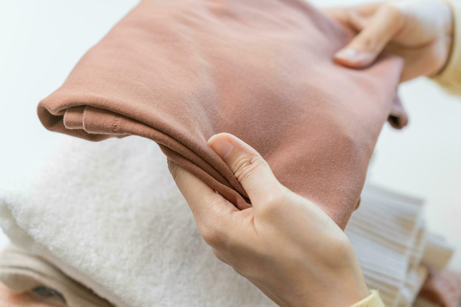 Feel softness, asian young woman, girl hand in holding pile, stack folding clean clothes after washing, laundry and dry. Household working at home. Laundry and maid, close up on white background. photo