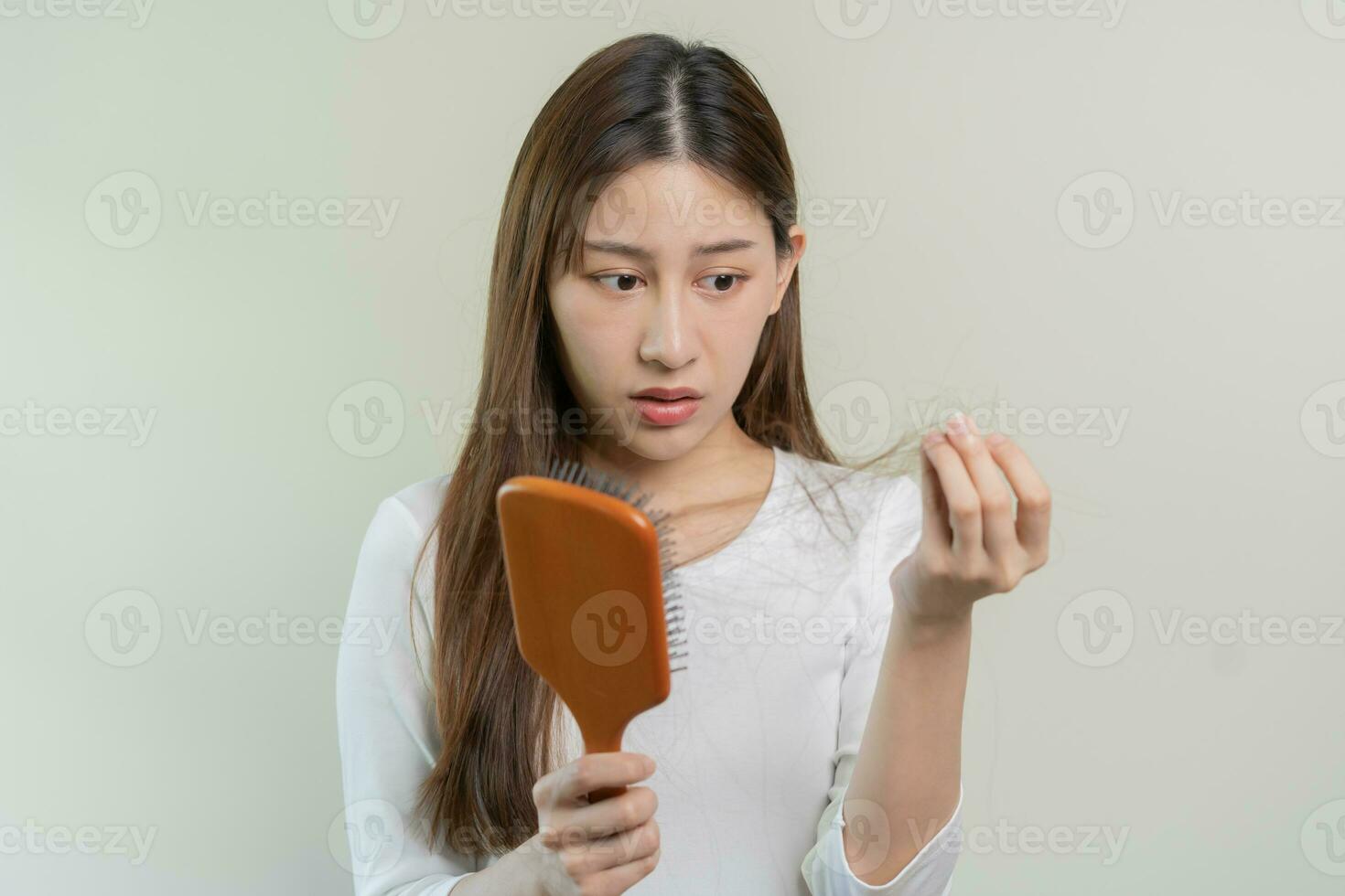 Serious, worried asian young woman, girl holding brush, show her comb, hairbrush with long loss hair problem after brushing, hair fall out on her hand in living room. Health care, beauty treatment. photo