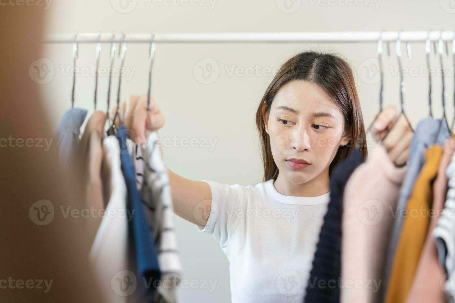 Choice of clothes,Nothing to wear. Attractive asian young woman, girl try on appare, happy choosing dress, outfit on hanger in wardrobe in room closet at home. Deciding blouse what to put on which one photo