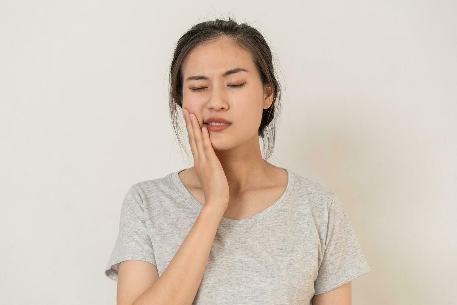 Closing eyes asian young woman touching cheek, face expression from toothache, tooth decay or sensitivity, Having tooth or teeth problem or inflammation, suffering from health. Sensitive teeth people photo