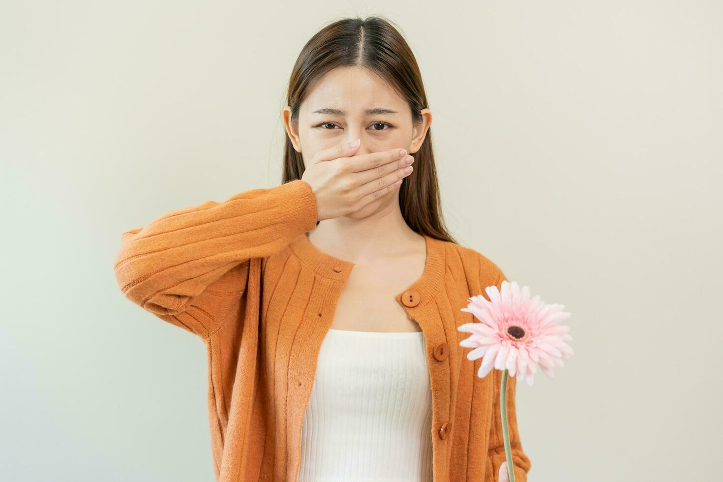 Allergic rhinitis symptom of odor pollen flowering, portrait asian young woman hand in sneeze, blowing runny nose after smell, smelly from bloom flower, holding away pink flora on white background. photo