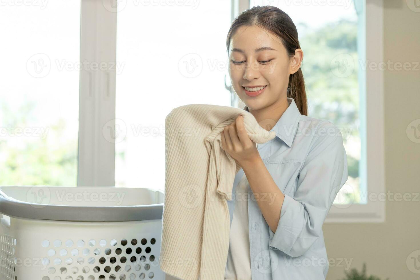 Feel softness, smiling asian young woman, girl touching fluffy towel cotton, smelling fresh clean clothes on table after washing, laundry, dry. Household working at home. Laundry and maid. photo