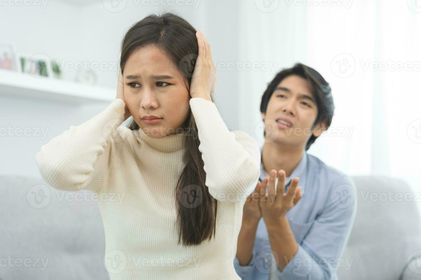 Breakup and depressed, asian young quarrel couple love fight relationship in trouble, woman cover ears. Argue wife has expression, upset with husband sitting together on sofa. Problem of family people photo