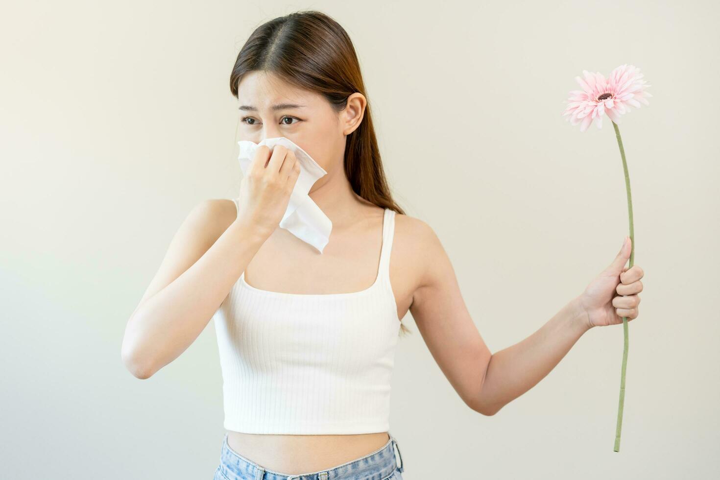 Allergic rhinitis symptom of odor pollen flowering, portrait asian young woman hand in sneeze, blowing runny nose after smell, smelly from bloom flower, holding away pink flora on white background. photo