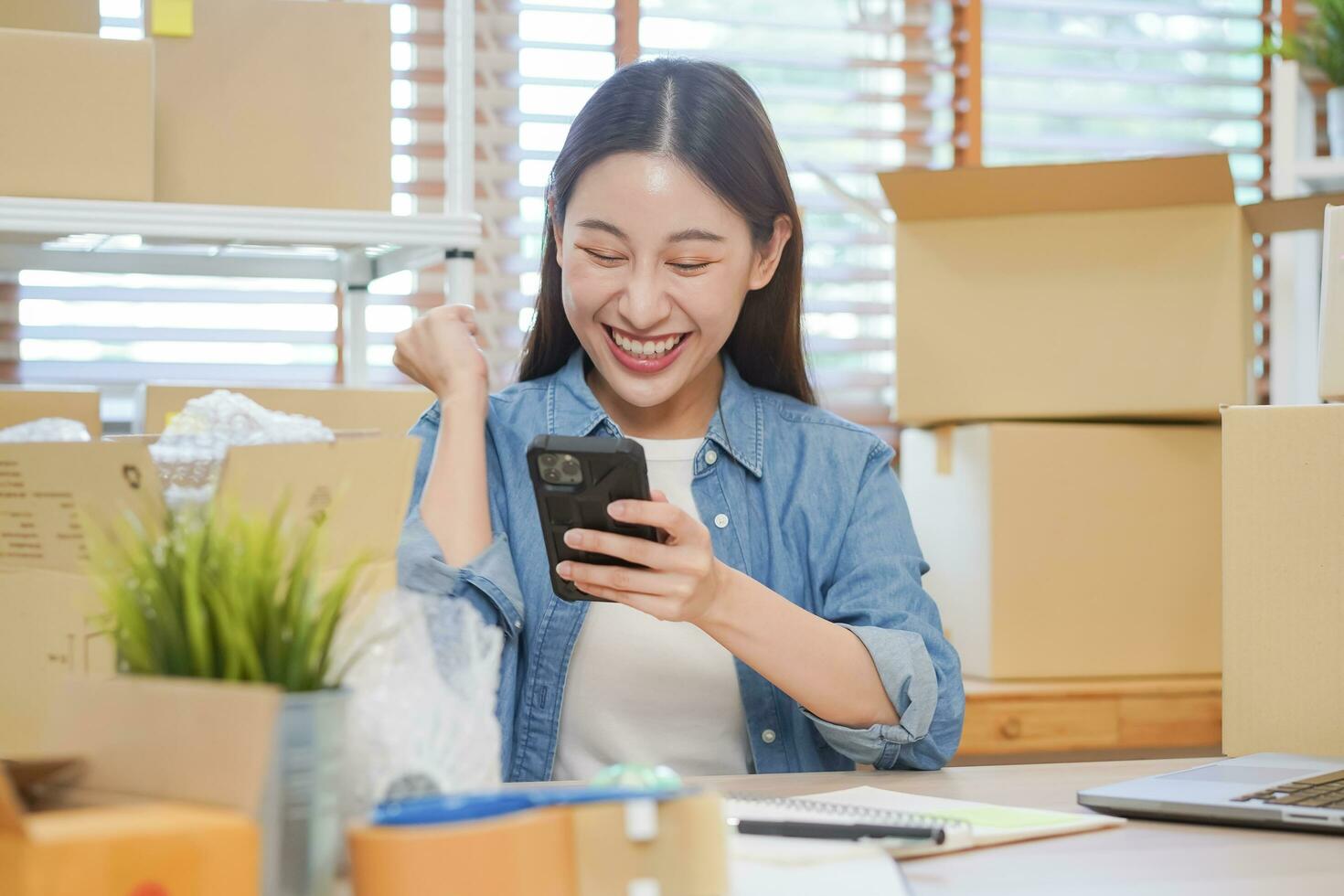 alegre pequeño negocio empresario pequeño, contento asiático joven mujer propietario sonrisa cuando recibir orden desde cliente en aplicación compras por teléfono inteligente, móvil. comerciante en línea, comercio electrónico trabajando a hogar oficina. foto