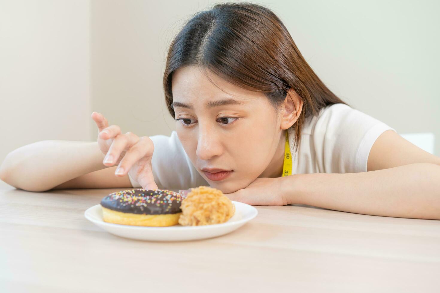 Diet, attractive asian young woman, girl restrained to eat doughnut, bakery and fried chicken, fast food to lose, loss weight, choose, choice eating on table at home. Passion, temptation when hungry. photo
