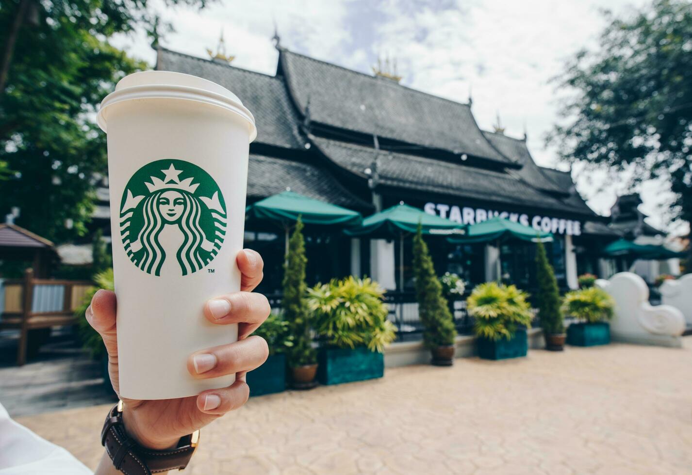 CHIANG MAI, THAILAND- July-24-2017 - Someone showing a cup of Venti size Starbucks hot coffee in front of of Starbucks Lanna style of Chiang Mai the northern province of Thailand. photo