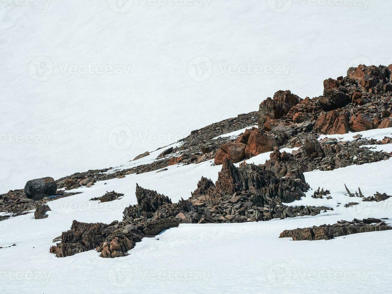 Highland scenery with sharpened stones of unusual shape. Awesome scenic mountain landscape with big cracked pointed stones closeup among snow under blue sky in sunlight. Sharp rocks. photo