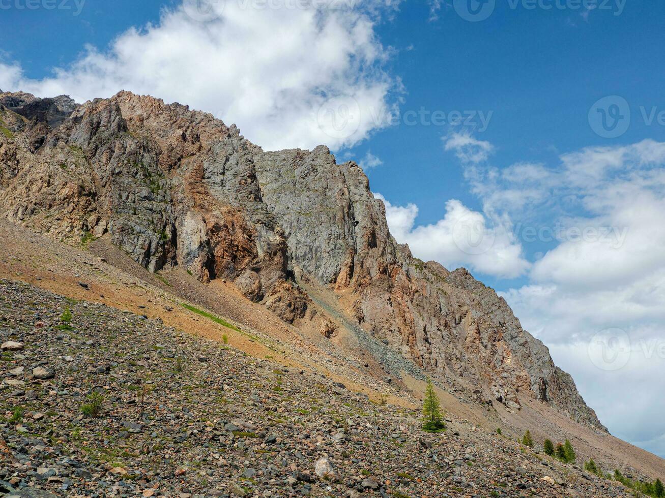 Atmospheric landscape with rocky mountain wall with pointy top in sunny light. Loose stone mountain slope in the foreground. Sharp stony mountains. photo