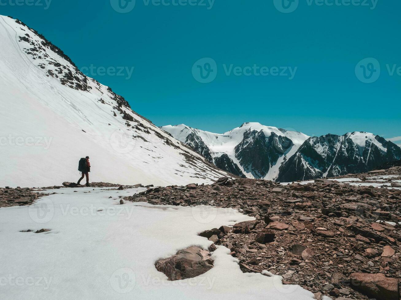 solo caminata a lo largo el nevadas montañas. extremo recreación y montaña turismo. un masculino caminantes abajo el montaña camino. en el fondo, grande nevadas montañas. foto