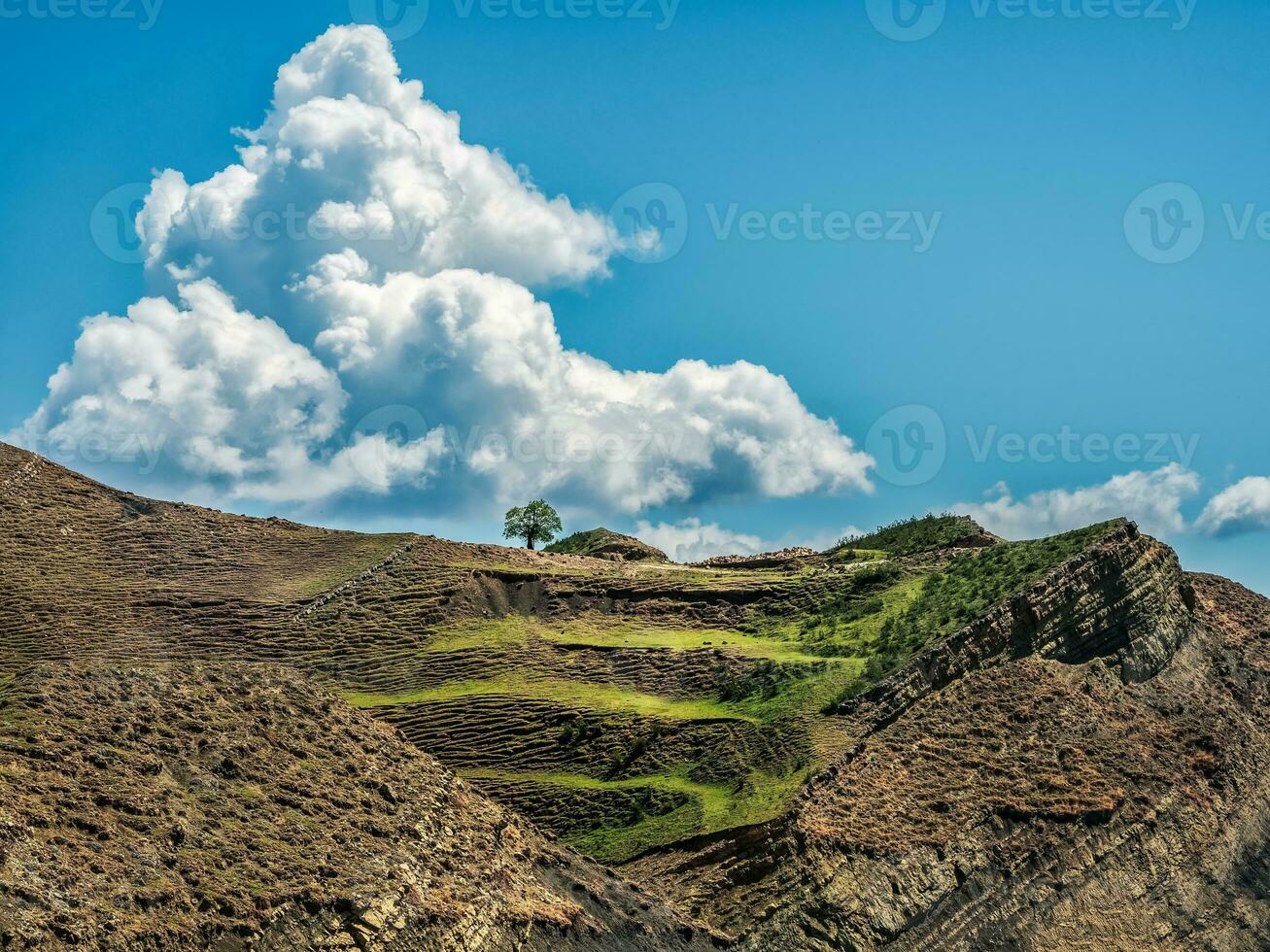 Bright white clouds in the sky and green terraces are covered with sparse vegetation of the slopes. High mountains, complex mountain landscape. photo