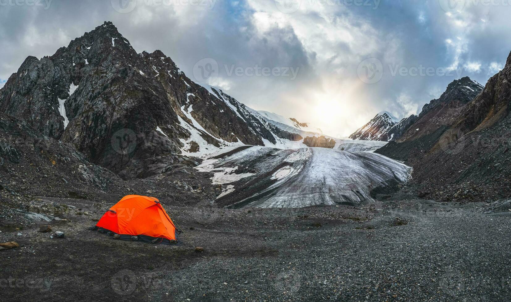 panorámico ver de un naranja fortificado tienda en el antecedentes de un glaciar en un alta altitud meseta. extremo durante la noche permanecer en el montañas. foto