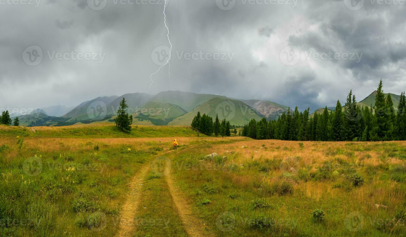 Single trekking in bad weather through a rainy mountain plateau. Figure of a tourist in a yellow raincoat on a mountain trail. photo