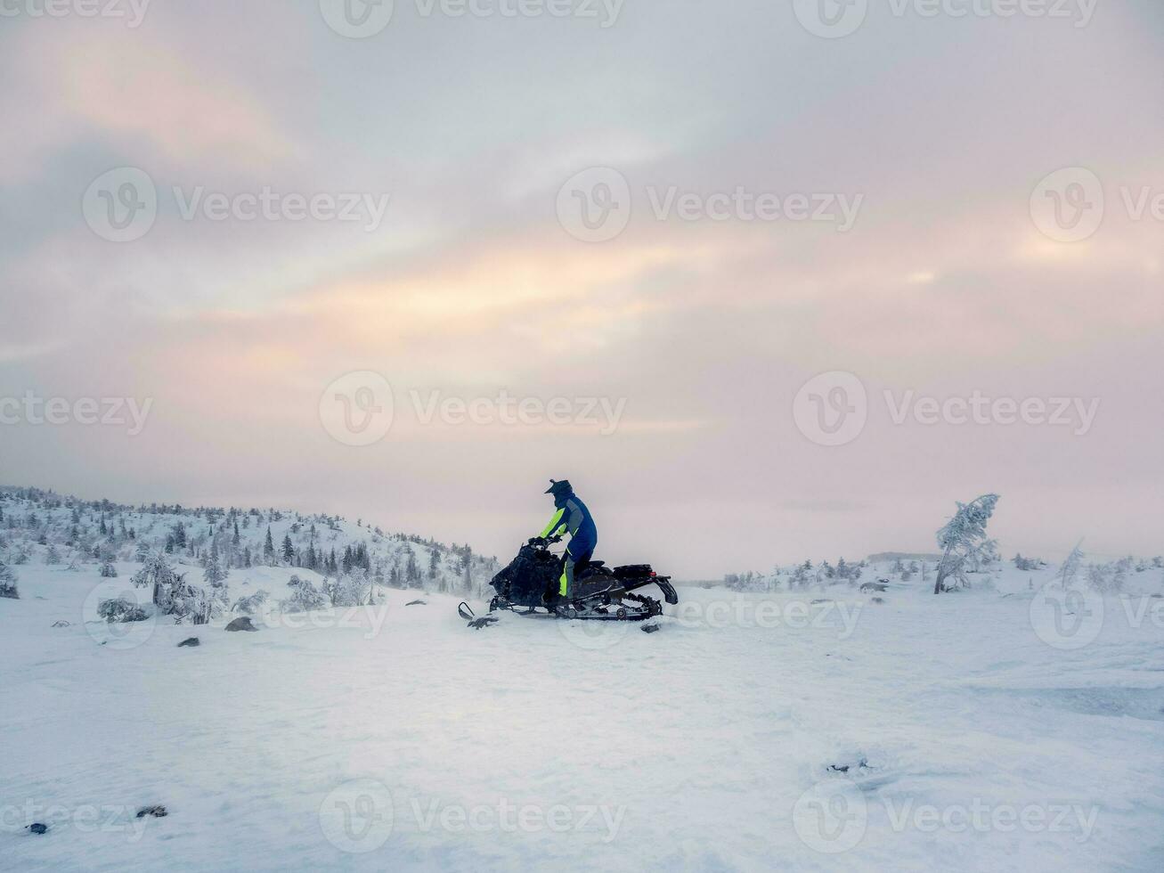 Male on snowmobile in the evening polar hill. Alone man riding up a hill on snowmobile. Extreme winter sports, polar active vacations in the harsh northern nature. photo