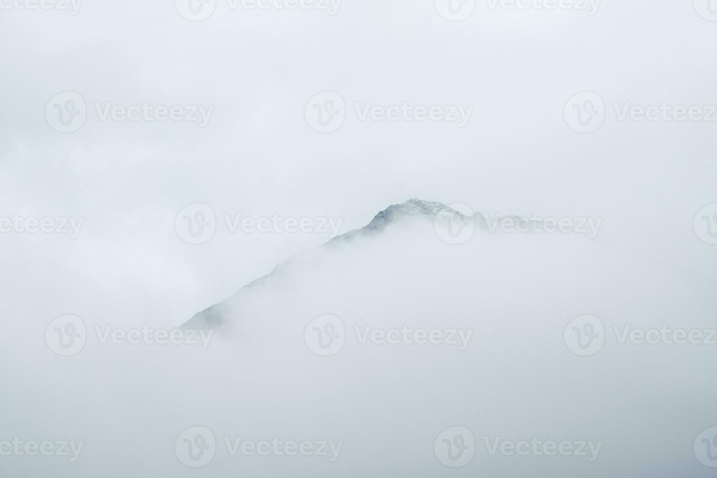 Soft focus. Wonderful minimalist landscape with big snowy mountain peaks above low clouds. Atmospheric minimalism with large snow mountain tops in cloudy sky. photo