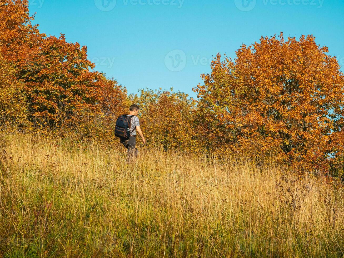 A middle-aged man with a backpack  coming down from the autumn hill photo