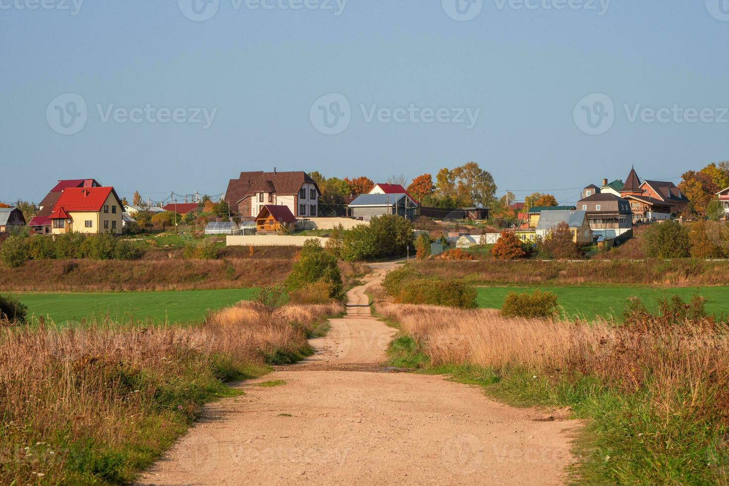 An empty dirt country road to a hill with cottages. photo
