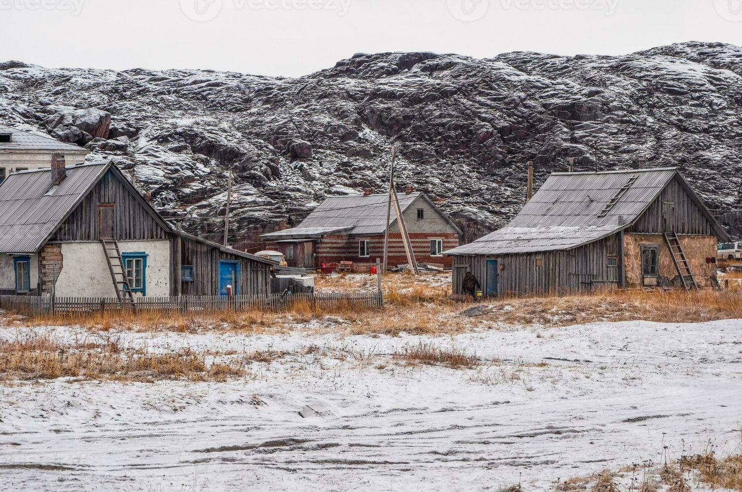 Clásico casas en el antecedentes de cubierto de nieve ártico sierras. antiguo auténtico pueblo de teriberka. kola península. foto