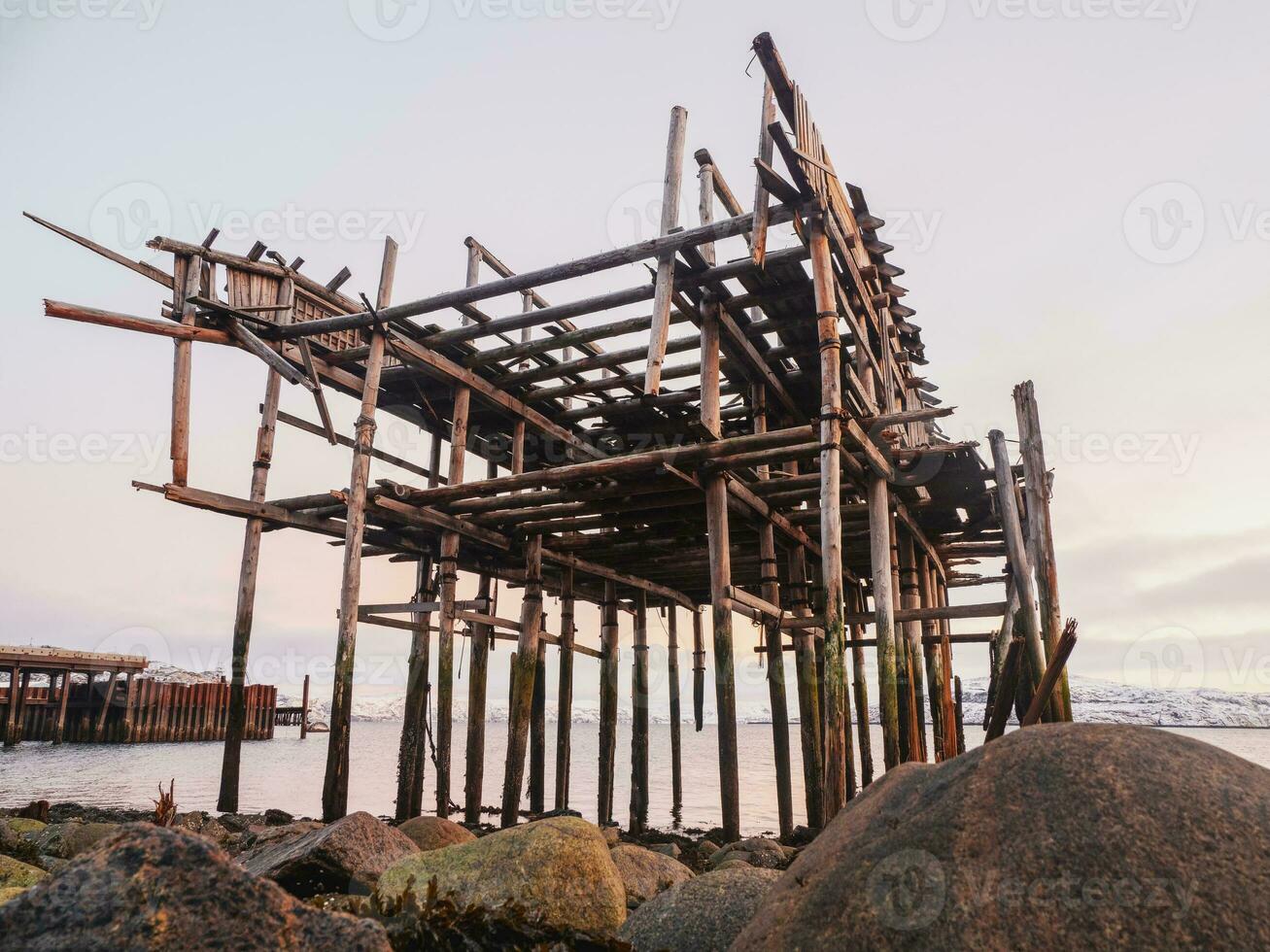 The skeleton of a fishing shed on the beach. Abandoned house against the Arctic sky. Old authentic village of Teriberka. photo