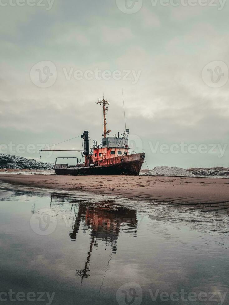 An old rusty fishing boat washed up on a sandy beach in the Barents Sea. Authentic the North sea. Teriberka. photo