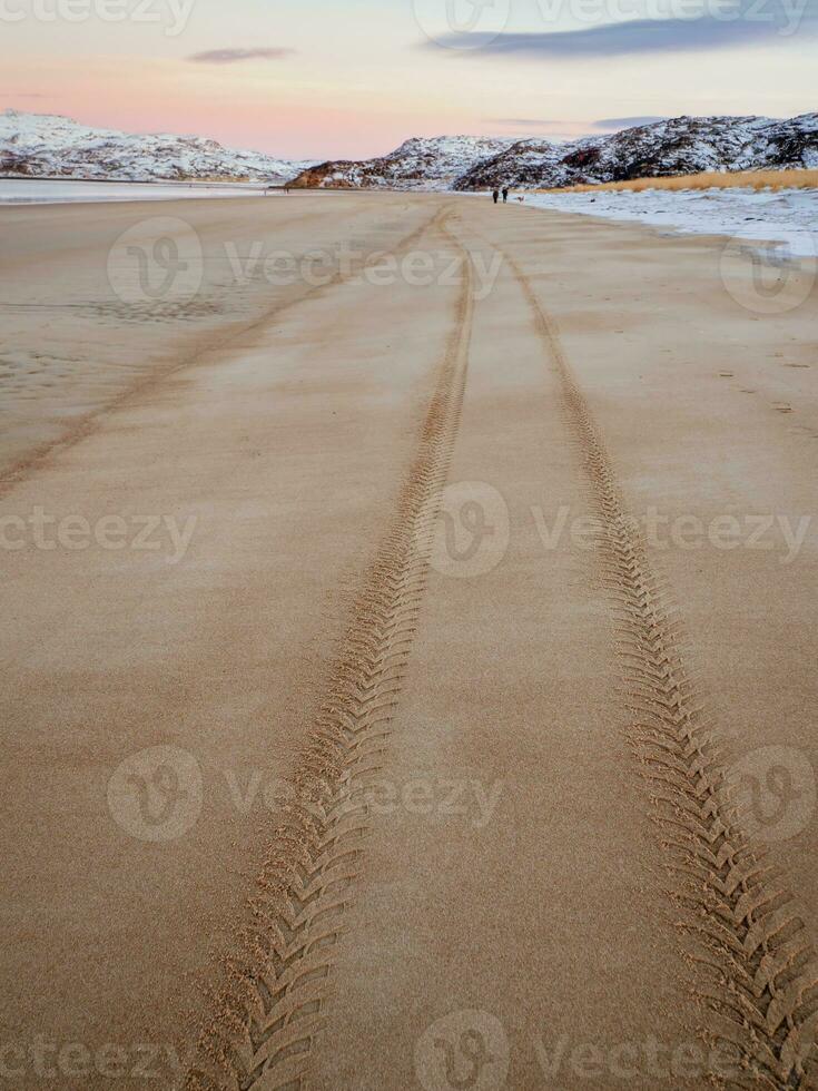 Tire tread mark on the sea sand extending into the distance photo