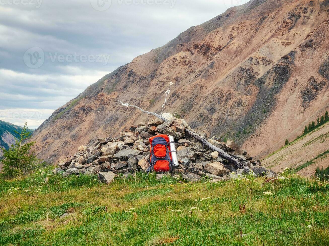 Large orange backpack on a pile of stones of an Alpine slope. Hiking in the highlands. Amazing bright mountain landscape of majestic nature. The time of the stop on the hike. photo