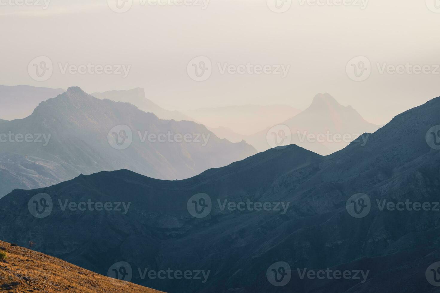 Scenic dawn mountain landscape with light fog in valley among mountains silhouettes under cloudy sky. Vivid sunset or sunrise scenery with low clouds in mountain valley in soft color. photo