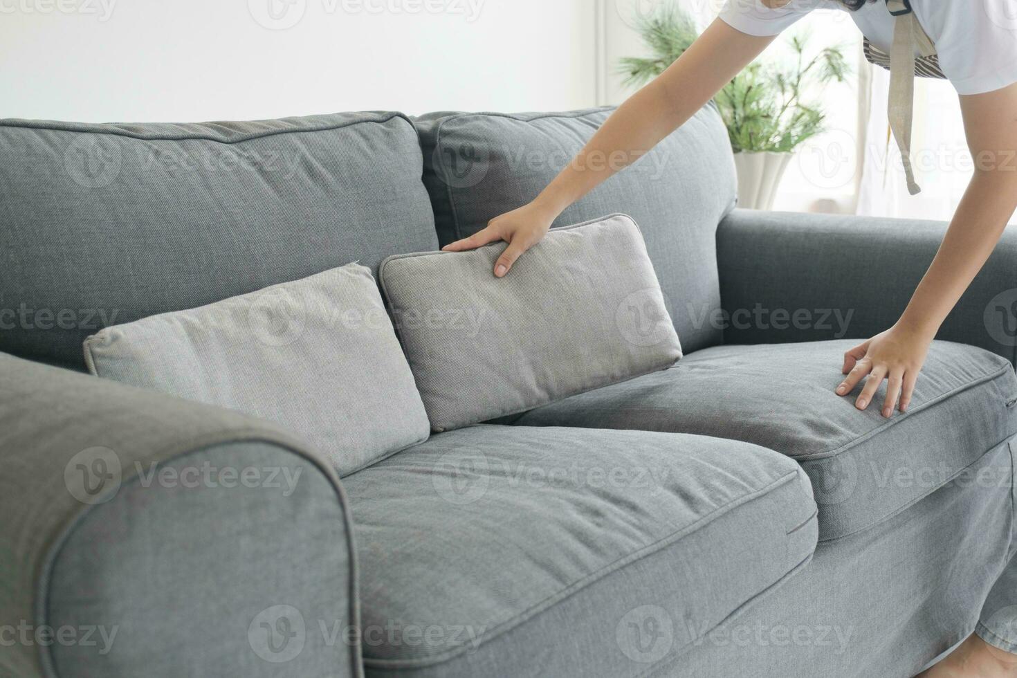 Woman cleaning and arranging sofa cushions at home. photo