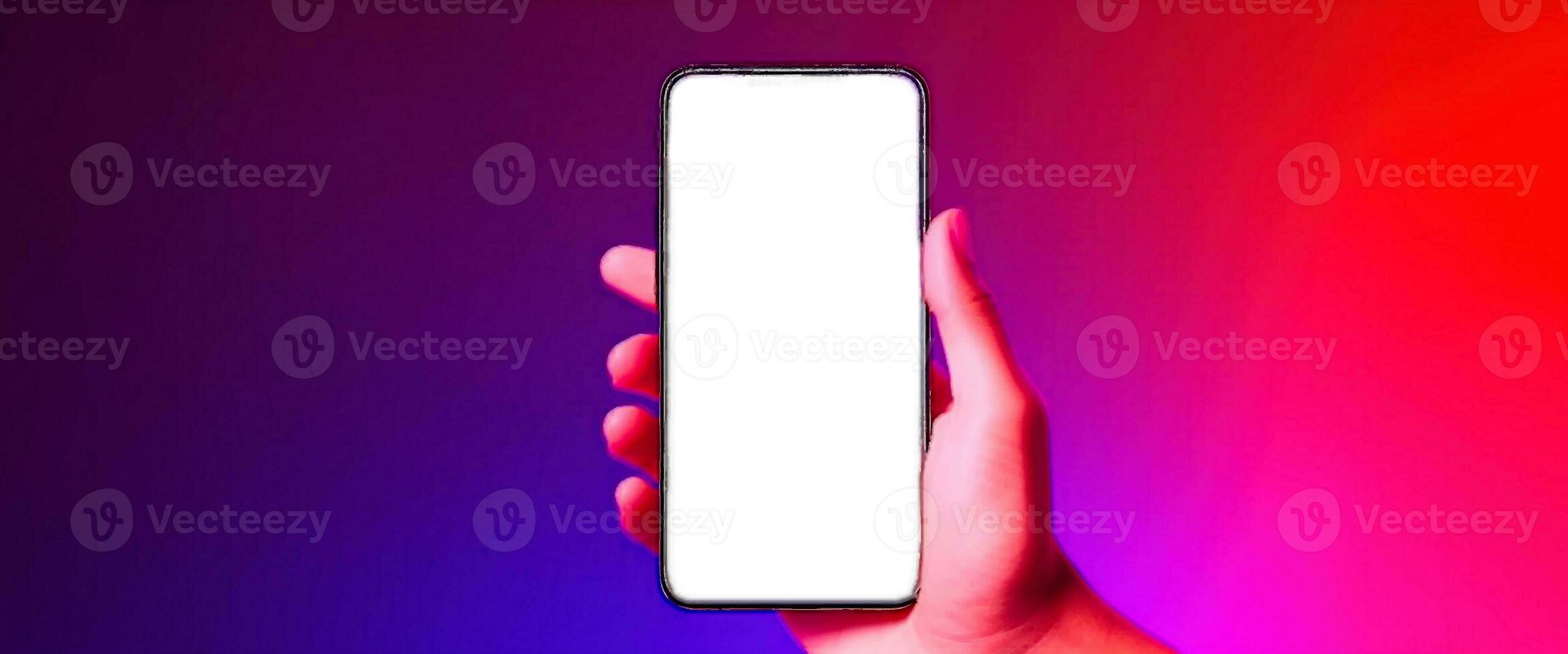 Phone in hand. Silhouette of male hand holding bezel-less smartphone with futuristic neon light on dark background. Screen is cut with clipping path. photo