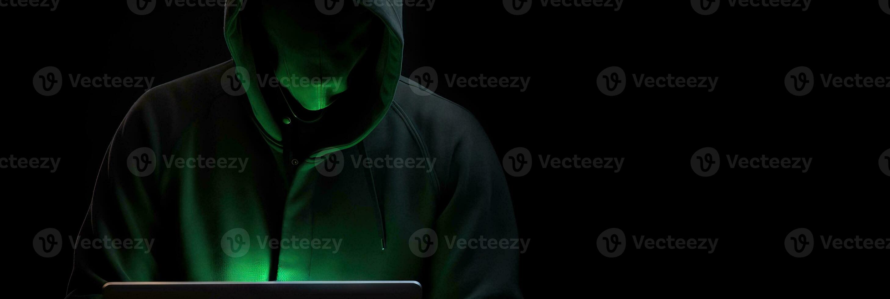 Hacker without face in a hood holds a laptop. on a dark background. Banner for cyber security.  Internet web hack technology. Digital laptop in hacker man hand isolated on black. photo