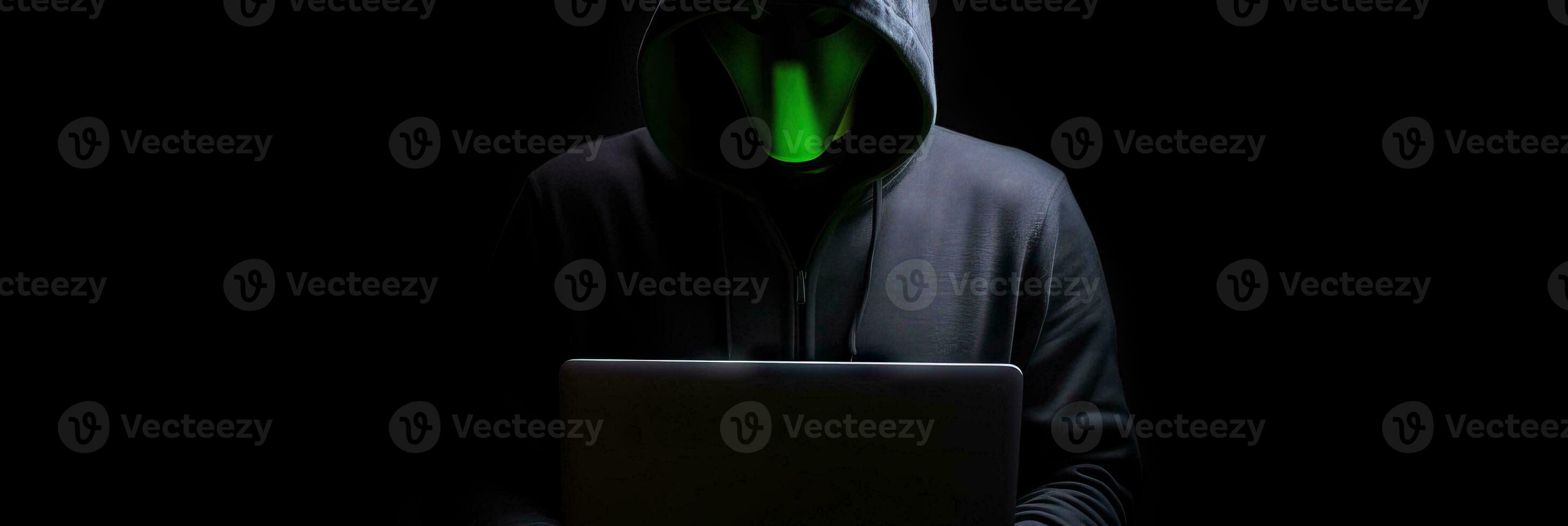Hacker without face in a hood holds a laptop. on a dark background. Banner for cyber security.  Internet web hack technology. Digital laptop in hacker man hand isolated on black. photo