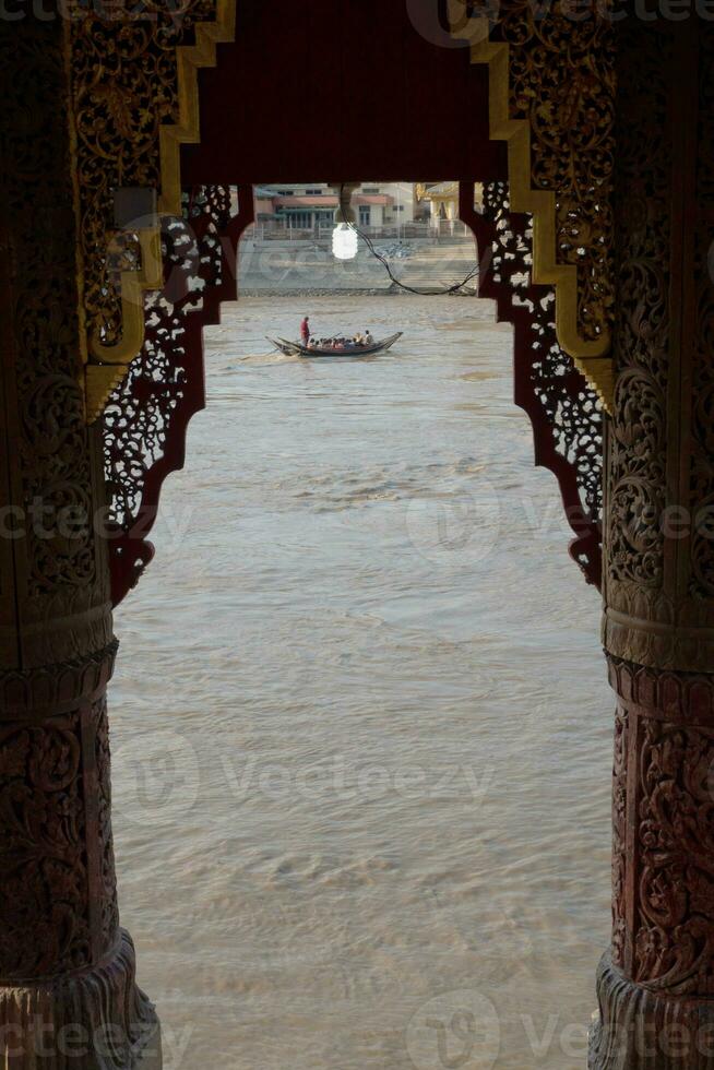 A passenger boat on the river in a frame that peers out between the pillars of the temple photo