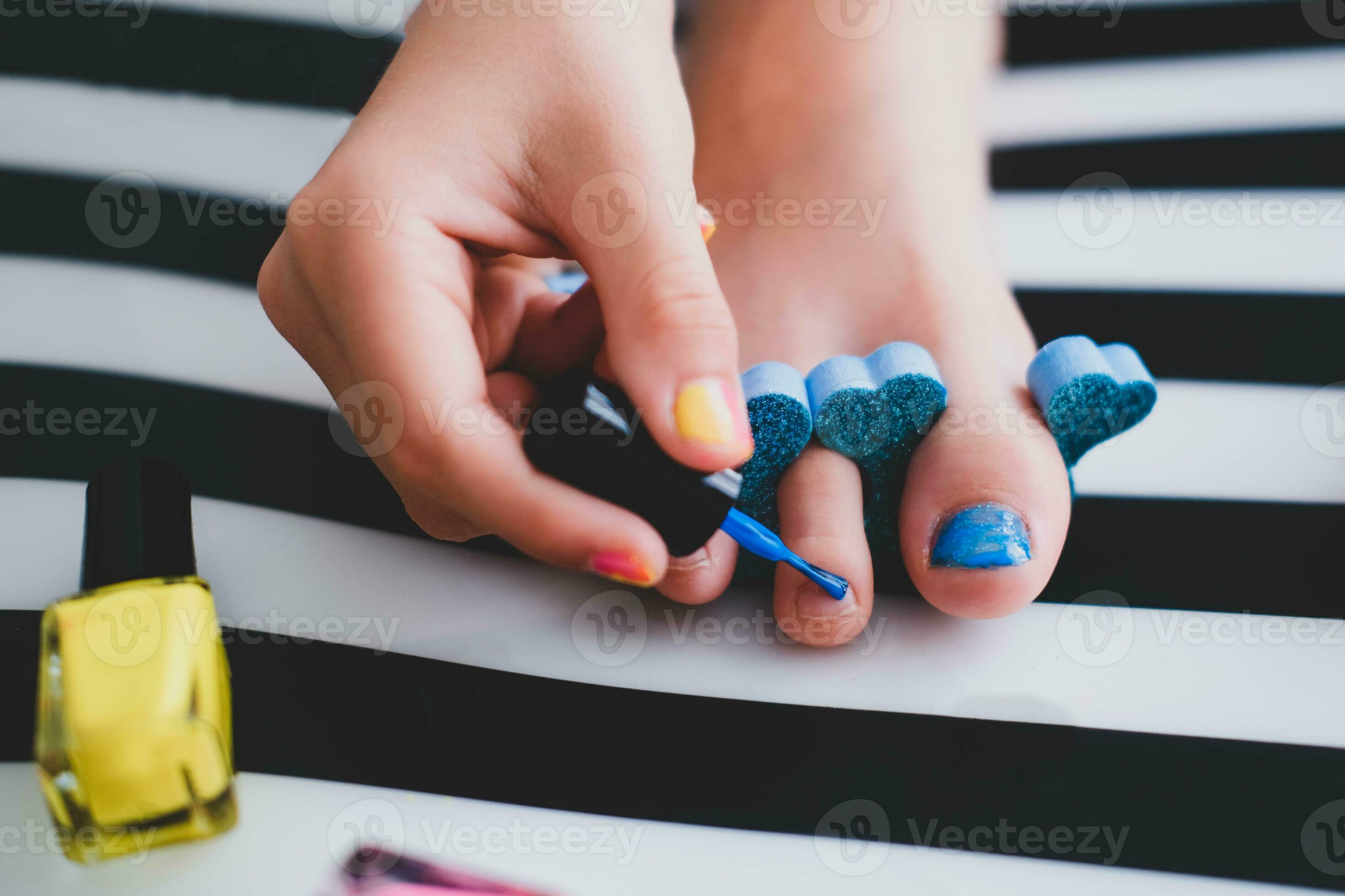 The child paints his toenails with bright blue varnish. Little girl
