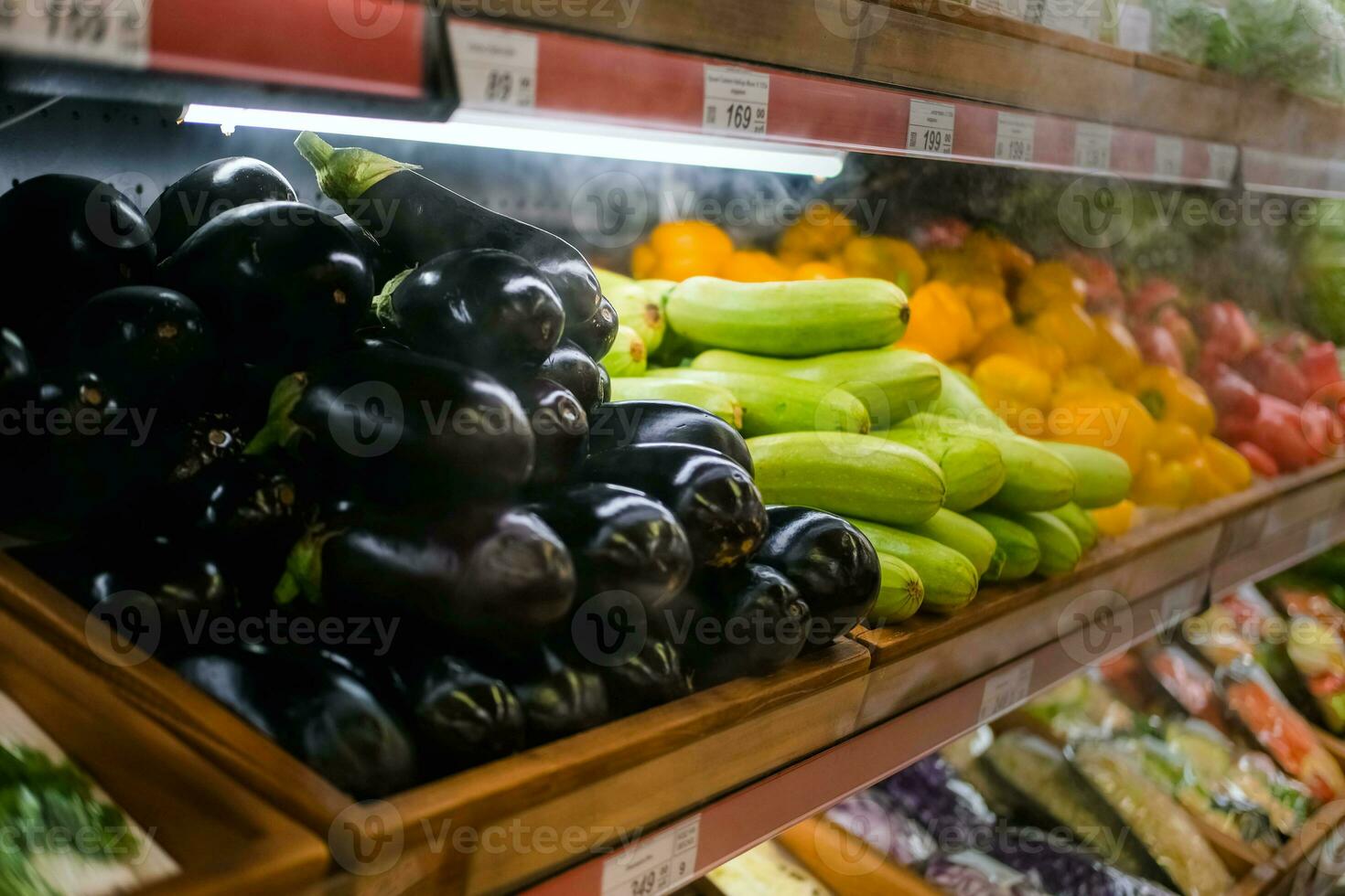 The grocery store sells various vegetables, tomatoes, cucumbers, eggplants, peppers, zucchini. Vegetables are on the shelf in the grocery store. photo