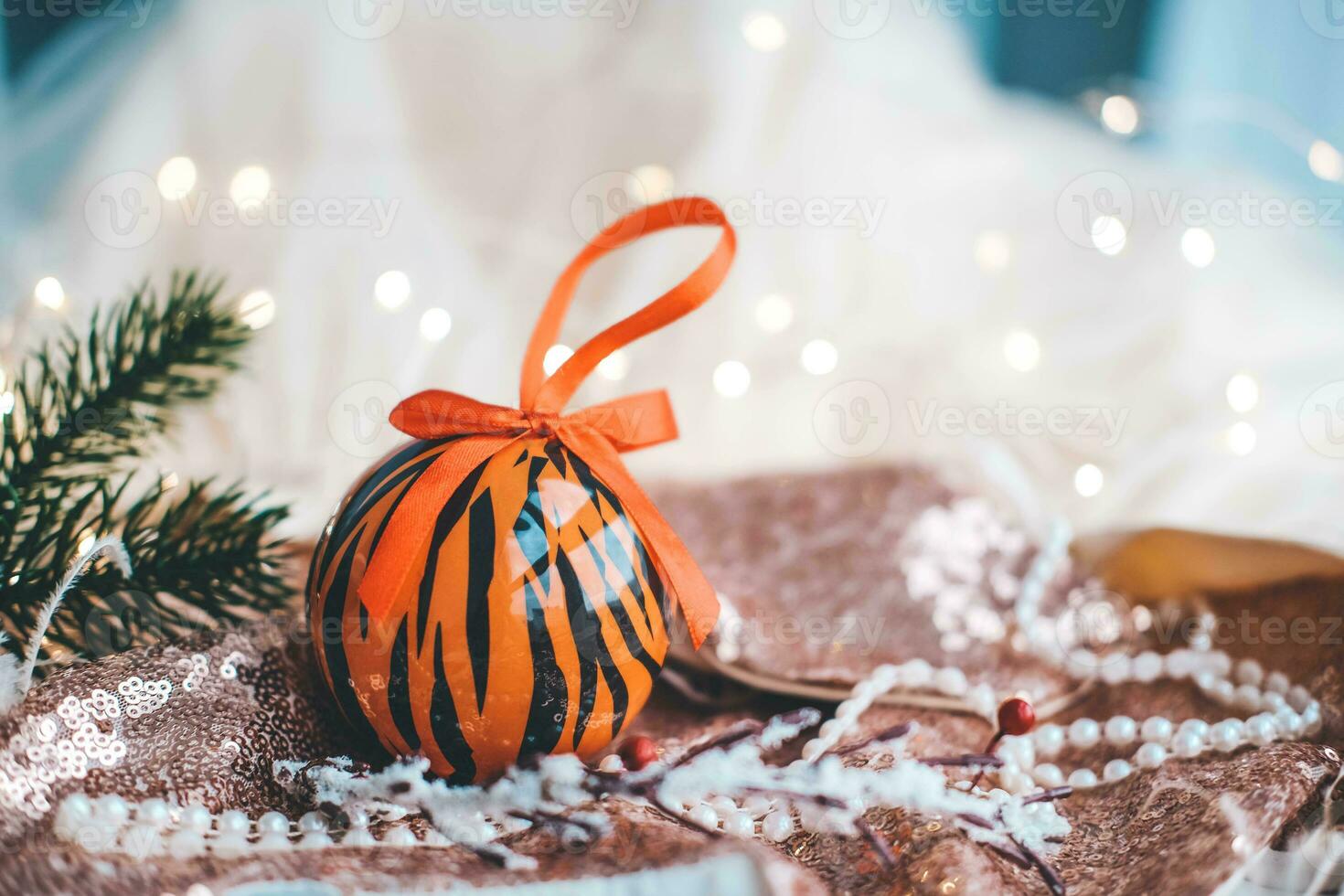 Christmas ball painted as tiger stripes spins on blurred christmas garland. background.  2022 is a year of the Tiger. Happy New Year . Symbol of year lunar chinese calendar tiger on Christmas  ball . photo