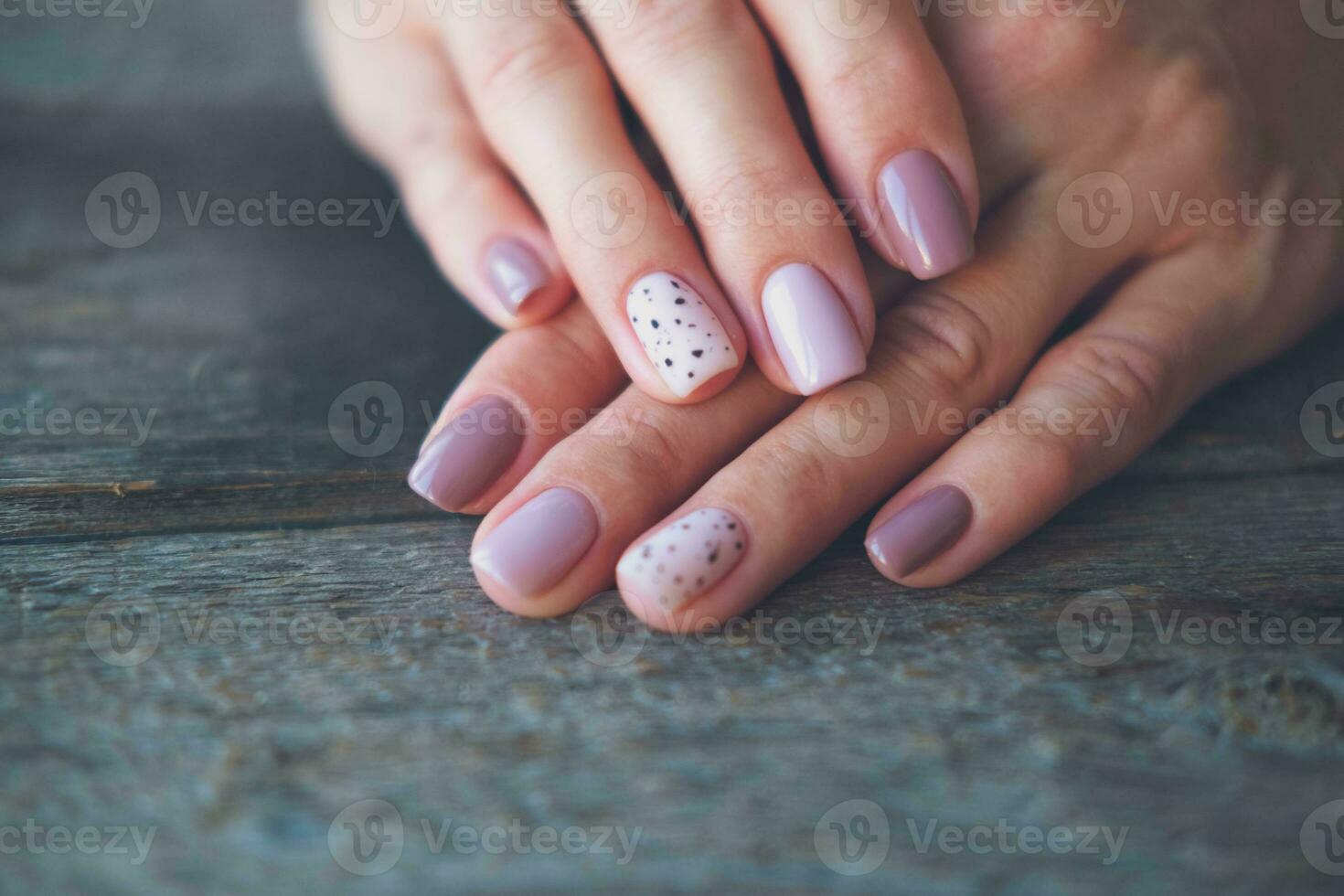 Women is hands with a beautiful manicure  on a wooden background. Autumn trend, polish the beige and quail egg pattern on the nails with gel polish, shellac. Copy space. photo