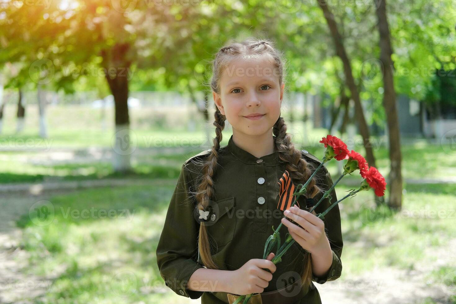 A girl in a special uniform with a St. George ribbon holds three carnations in her hands. Holiday Victory Day May 9th. photo