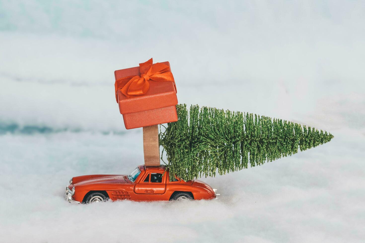 Krasnodar, Russia - December 10, 2019 Red toy car with a gift on the roof, rides in the snow. Delivery of gifts. Copy space. Christmas . New year. photo