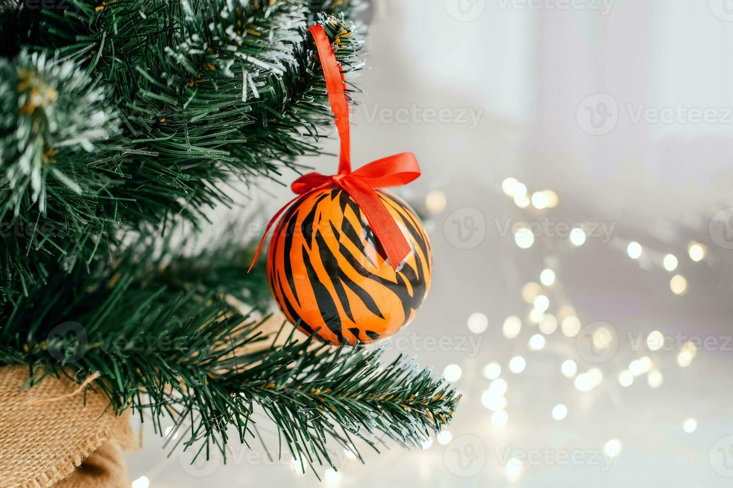 Christmas ball painted as tiger stripes on Christmas tree with a garland. 2022 is a year of the Tiger. Happy New Year . Symbol of year lunar chinese calendar tiger on Christmas ball. photo