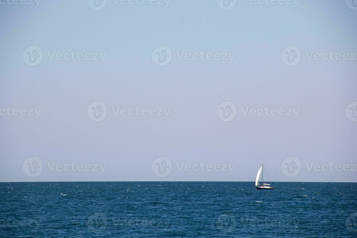 Small sailing yacht with big white sails in the open sea on the horizon photo