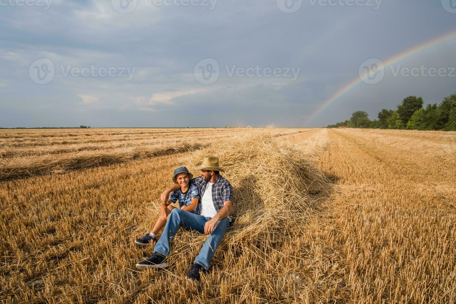 padre y hijo son en pie en su trigo campo después un exitoso cosecha. foto