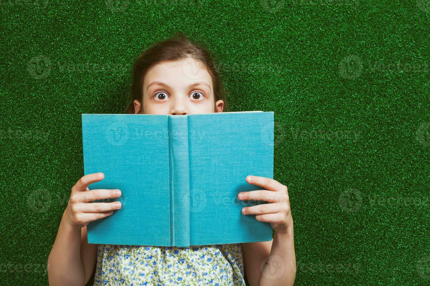 Little girl is lying on artificial grass with a book photo